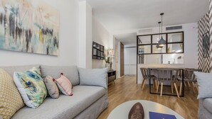 A modern living room with a grey sofa, a coffee table, and a dining area with a wooden table and chairs. - Design apartment next to La Maestranza & Cathedral (Sevilla)