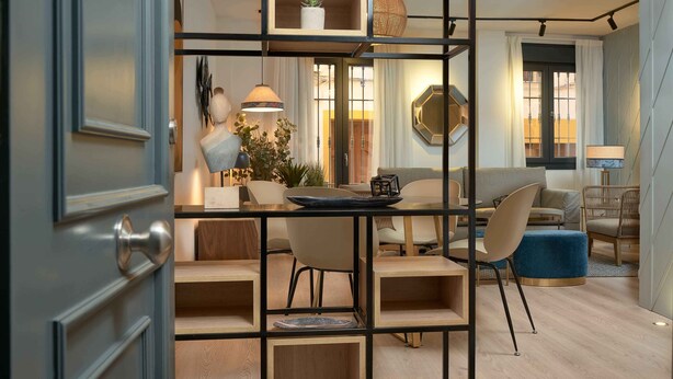 Una sala de estar moderna con piso de madera, un comedor con mesa y sillas, y una zona de estar con sofás y un otoman azul.