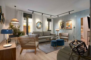 A modern living room with a sofa, a wicker chair, a glass coffee table, and a blue ottoman. There are two pendant lights, a floor lamp, and a geometric sculpture on the coffee table. - Modernity & luxury a few steps from everything in Seville (Sevilla)
