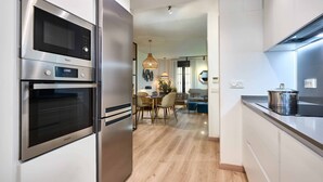 Una cocina moderna con electrodomésticos de acero inoxidable, un comedor con mesa y sillas de madera, y vistas al salón.