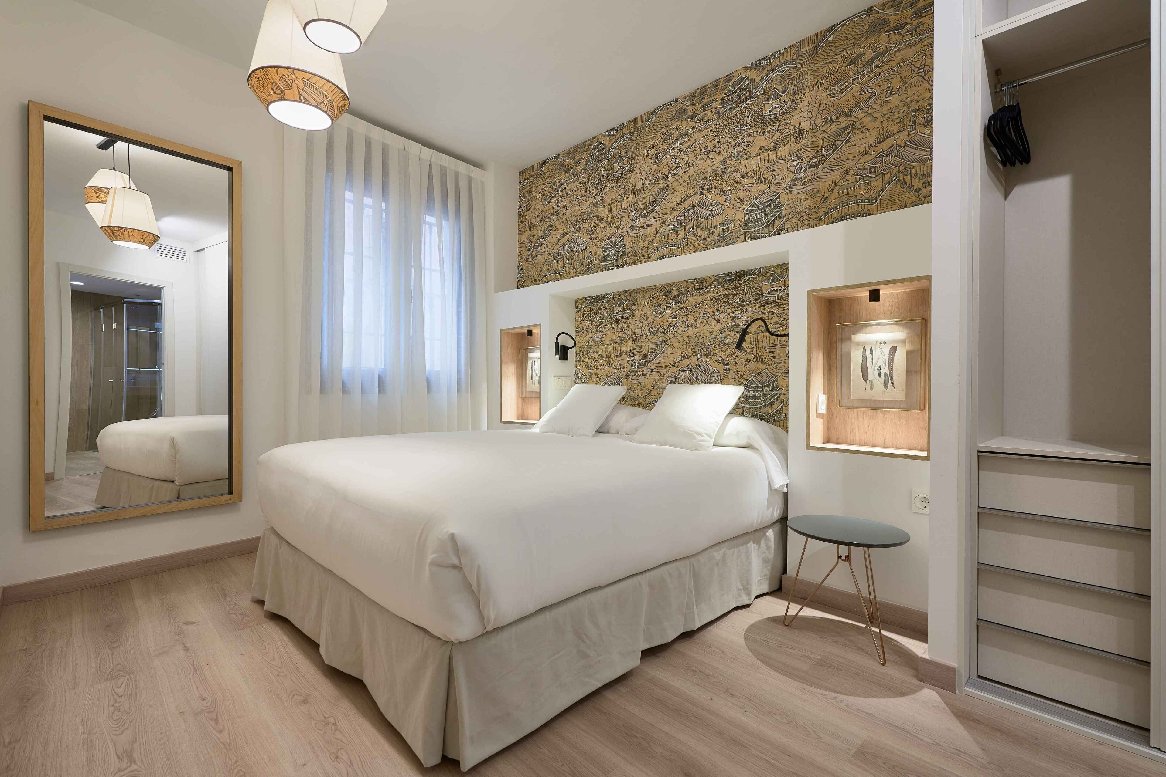 A bedroom with a large bed, a mirror, a wall-mounted light, and a patterned wall.