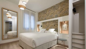 Un dormitorio con una cama grande, un espejo, una lámpara de pared y un papel tapiz estampado.