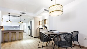 Una cuina moderna amb zona de menjador, que destaca per una illa central amb tamborets, una taula rodona amb cadires, il·luminació penjant i un llum de sostre amb disseny.