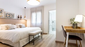 Habitació d'hotel moderna amb un llit gran, un escriptori i una cadira. Hi ha una finestra amb cortines, una taula de nit amb una làmpada i una obra d'art a la paret.