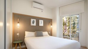 A bedroom with a large bed, a small side table, a wall-mounted air conditioner, and framed botanical prints. - Amador de los Rios Free Parking Gratis (Sevilla)