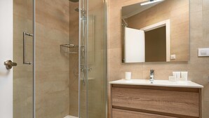A modern bathroom with a glass-enclosed shower, a wooden vanity with a mirror, and a white countertop. - Amador de los Rios Free Parking Gratis (Sevilla)