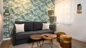 A modern living room with a dark grey sofa, two round wooden tables, and a patterned wallpaper. - Amador de los Rios Free Parking Gratis (Sevilla)