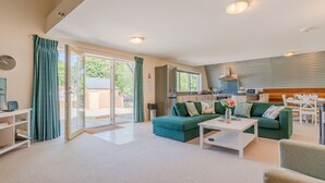 Ein modernes Wohnzimmer mit einer Couch, einem Couchtisch und einem durch eine Glastür einsehbaren Küchenbereich.