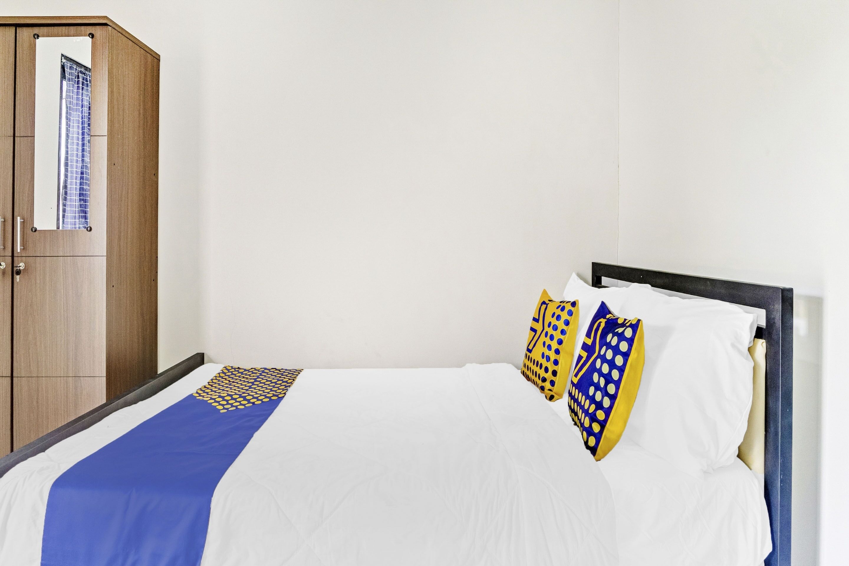 A bedroom with a bed, a wooden wardrobe, and a mirror.