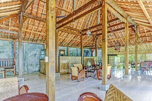 Una habitación amplia con un alto techo de madera, suelo de baldosas y varias sillas y mesas de madera.