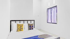 A bedroom with a bed, white walls, a window with curtains, and a bedspread with a blue and yellow pattern. - SPOT ON 90742 Kinanthy Homestay Syariah (Tulungagung)