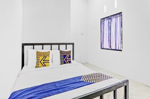Un dormitorio con cama, paredes blancas, ventana con cortinas y edredón estampado en azul y amarillo.