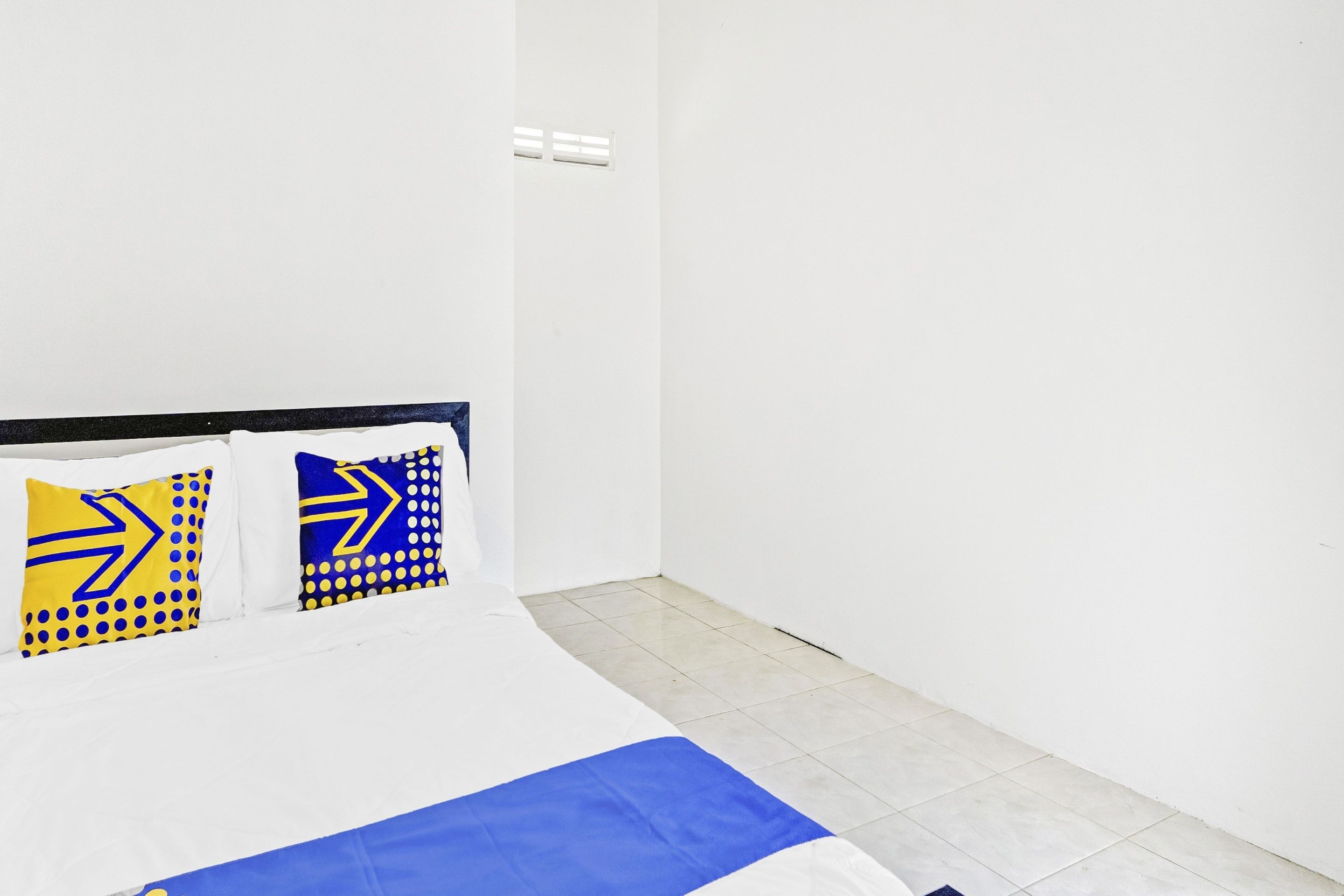 A bedroom with a bed, white walls, and a tiled floor.