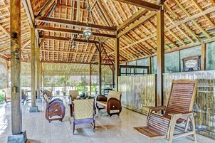 Un espacio de estar al aire libre cubierto, con mobiliario de madera y suelo de baldosas.
