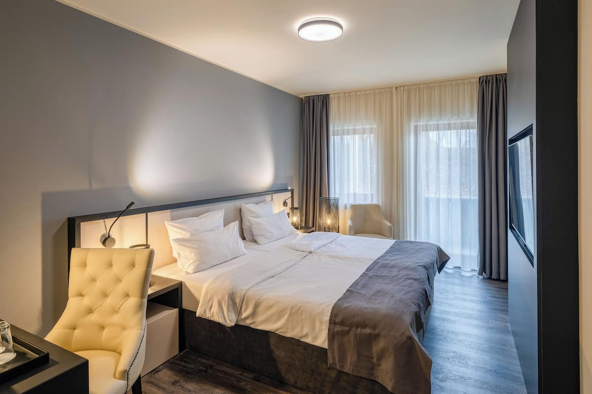 Une chambre d’hôtel avec un lit, une chaise, un bureau et une fenêtre avec des rideaux.