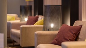 Un espace de détente moderne avec des canapés et une table ronde, agrémenté d’œuvres d’art aux murs et d’une lampe à motifs.