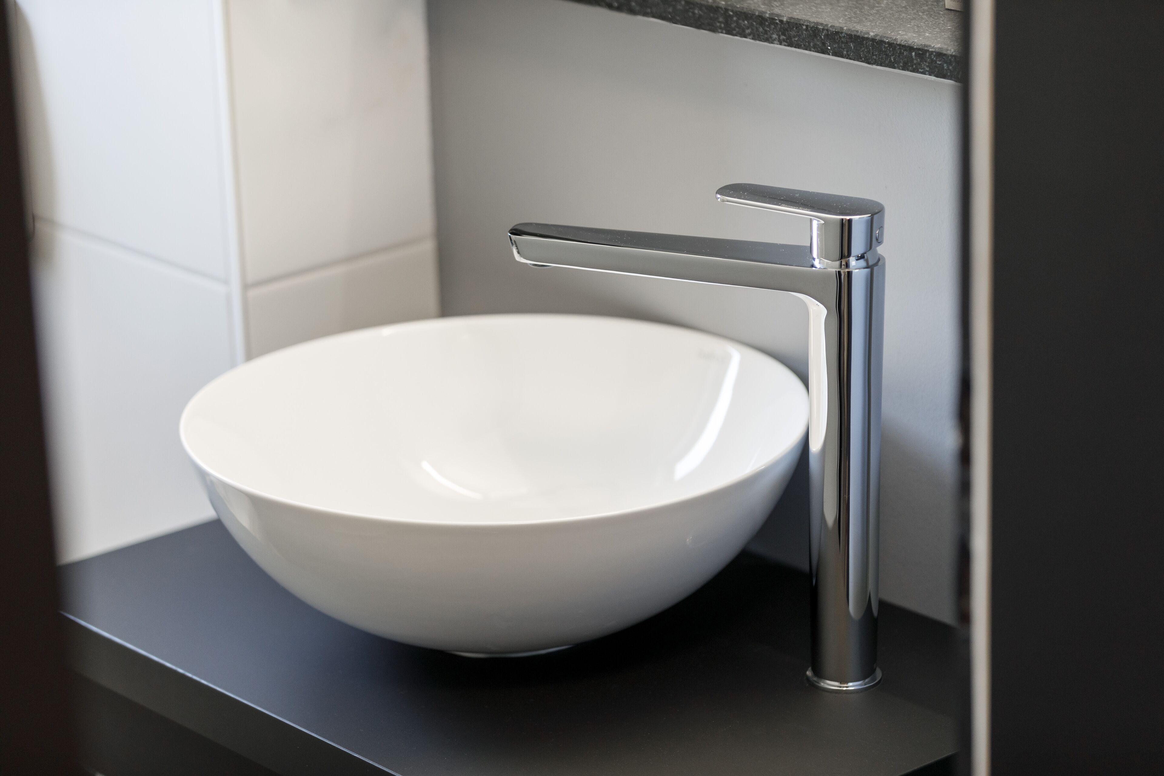 Un lavabo in ceramica bianca con un rubinetto cromato montato su un piano di lavoro nero.