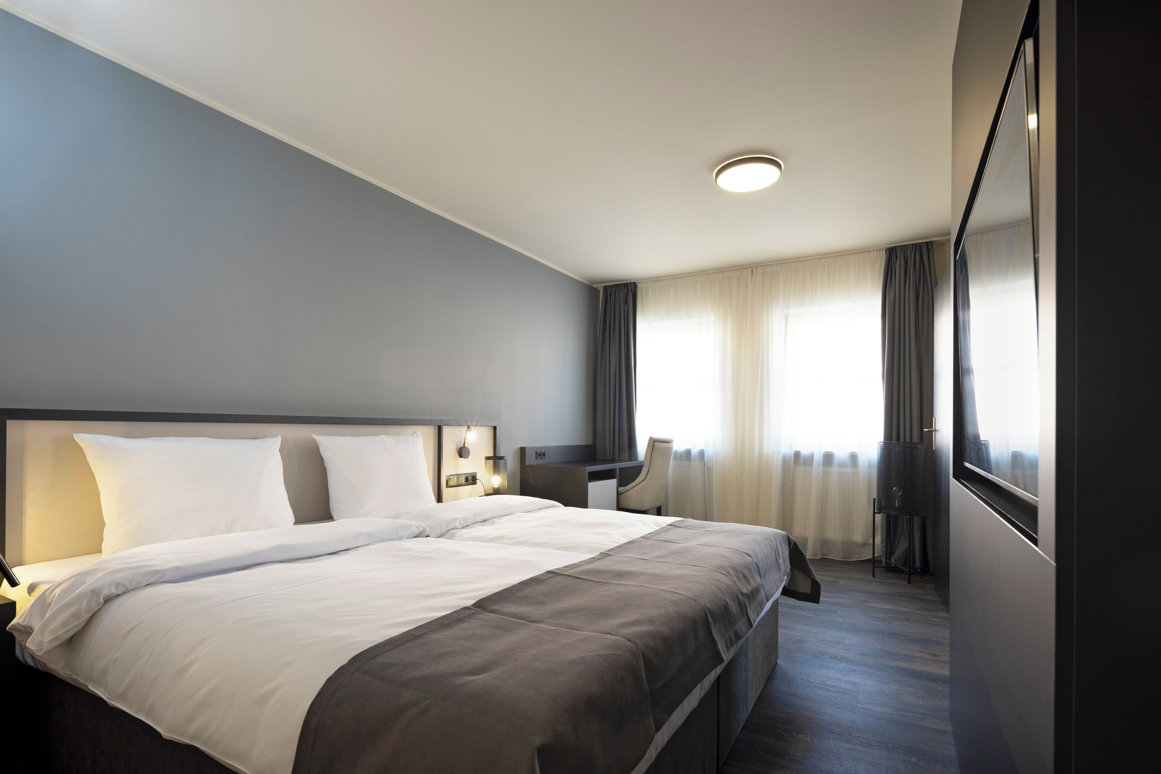 A hotel room with a large bed, a desk, and a chair.
