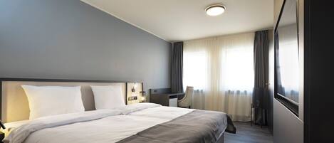 A hotel room with a large bed, a desk, and a chair.
