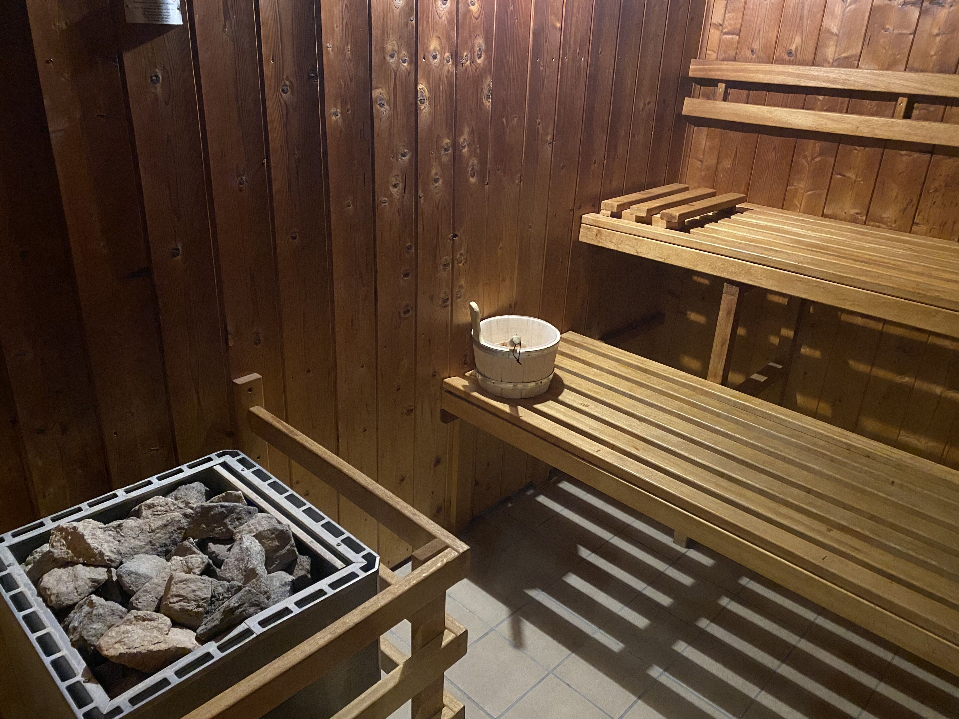 A sauna with wooden benches, a stone heating element, and a white bucket.