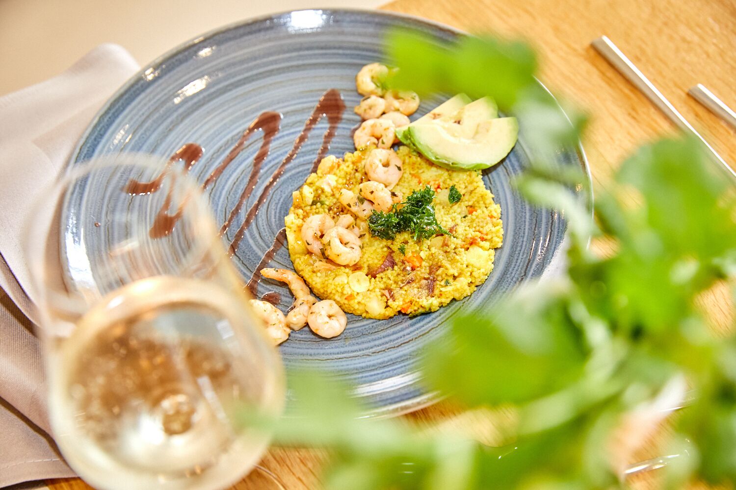 A plate of food with shrimp and avocado on a blue plate, accompanied by a glass of wine.