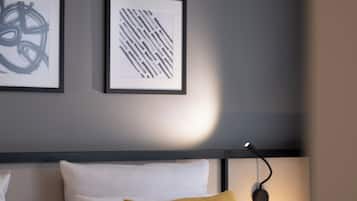 A neatly made bed with white and mustard pillows, a headboard, and two framed abstract artworks on the wall.