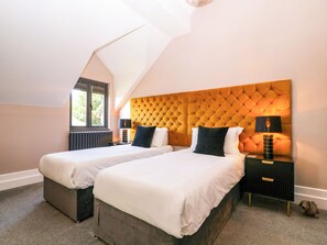 Un dormitorio con dos camas, una ventana, un radiador y una mesita de noche con una lámpara.