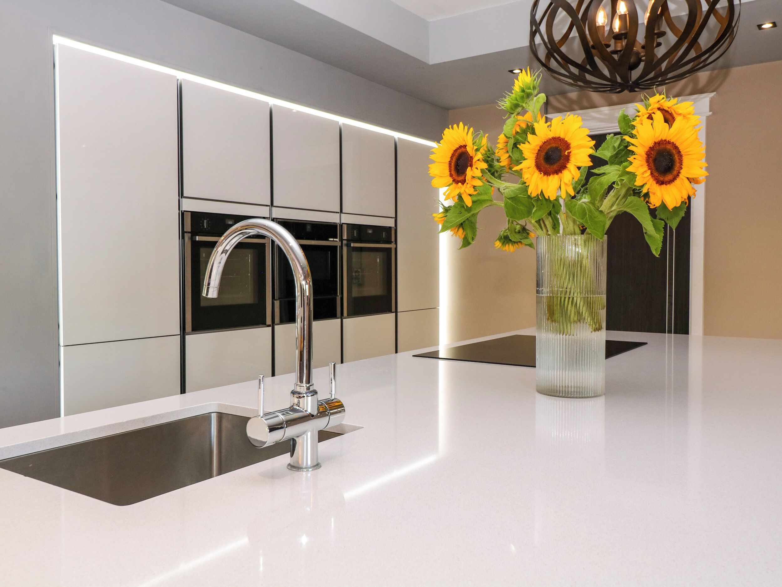 A modern kitchen with a stainless steel faucet, a built-in oven, and a vase with sunflowers on the countertop.