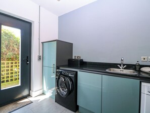 Cocina compacta con lavadora, lavamanos y puerta que da a un balcón.