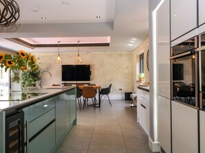 A modern kitchen with a central island, a dining area with chairs, and a TV mounted on the wall. - Thornbury (Malvern)