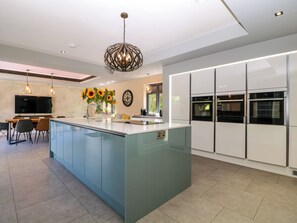 A modern kitchen with a central island, built-in ovens, and a dining area with chairs and a table. - Thornbury (Malvern)