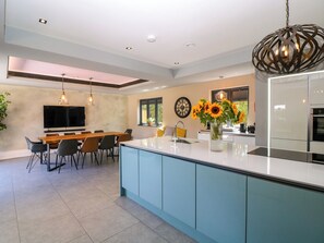 Cocina moderna con una isla central, comedor con sillas, televisor de pantalla plana en la pared y un ventanal con vistas.