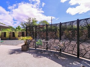 Un patio con cerramiento metálico decorativo, mobiliario exterior y plantas en macetas.