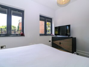 Un dormitorio con una cama, un televisor sobre un mueble y dos ventanas.
