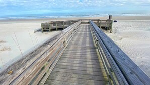 A wooden boardwalk leading to a beach with sand and ocean in the background. - Beautiful 6th floor, cathedral ceiling, ocean view condo (Pawleys Island)