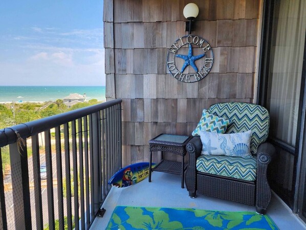 A balcony with a wicker chair, a small table, and a 'Welcome to the Beach' sign. - Beautiful 6th floor, cathedral ceiling, ocean view condo (Pawleys Island)