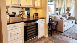 A kitchen with white cabinets, a black countertop, and a built-in dishwasher. There is a dining area with a sofa and a table, and a sign that reads "home sweet home." - Beautiful 6th floor, cathedral ceiling, ocean view condo (Pawleys Island)