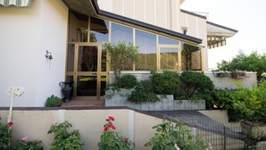 A modern house with a large glass door, a small porch, and a garden with various plants and flowers. - Appartamento La Fenice (Salò)