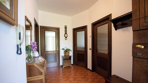 A hallway with wooden doors, a clock, and a vase with flowers. - Appartamento La Fenice (Salò)
