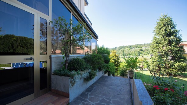 A modern building with large glass windows and a stone-paved patio. - Appartamento La Fenice (Salò)