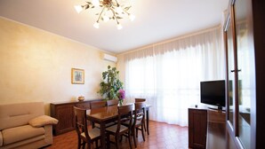 A living room with a sofa, dining table, chairs, a TV, and a plant. - Appartamento La Fenice (Salò)