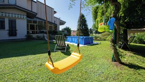 A backyard with a yellow swing, a blue play structure, and a white house in the background. - Appartamento La Fenice (Salò)