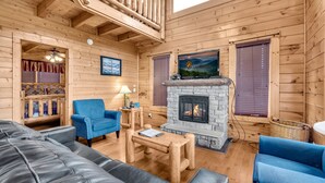 A log cabin interior with a fireplace, blue armchairs, a leather sofa, and a television displaying 'BearCamp'. - Aurora, Free Tickets, Breathtaking Views, “Cozy Cabin Retreat in the Smokies!!! (Sevierville)
