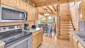 A wooden cabin kitchen with a large microwave, stove, and coffee maker. There is a dining area with a table and chairs. - Aurora, Free Tickets, Breathtaking Views, “Cozy Cabin Retreat in the Smokies!!! (Sevierville)