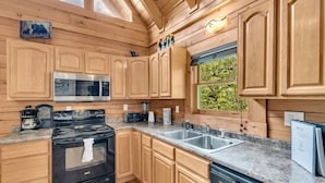 A wooden cabin kitchen with a stove, microwave, sink, and wooden cabinets.
