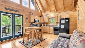 A wooden cabin interior with a kitchen, dining area, and a sofa.