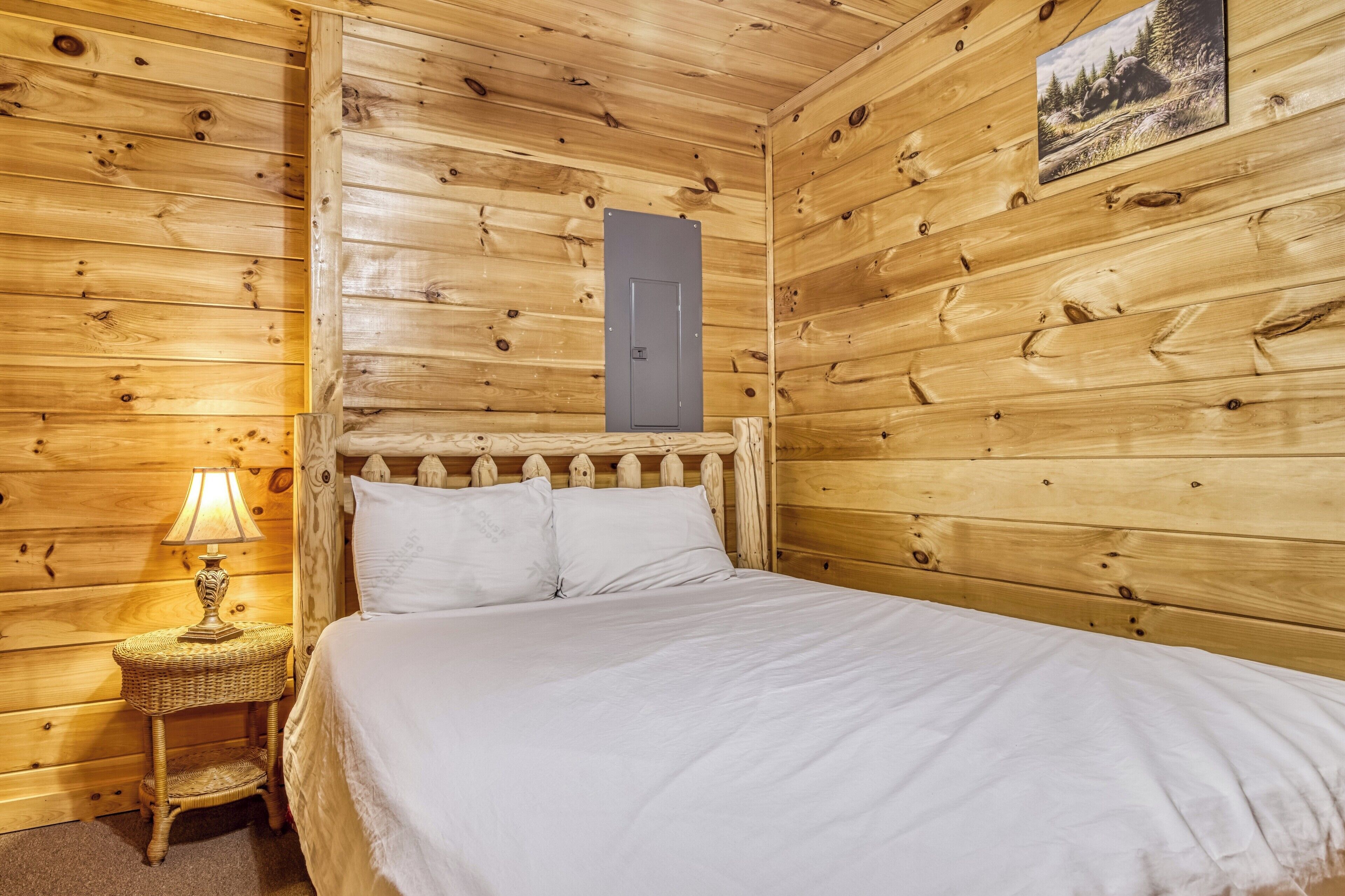Ein Holzhütten-Zimmer mit einem Bett, einem Nachttisch mit Lampe und einer Tür.