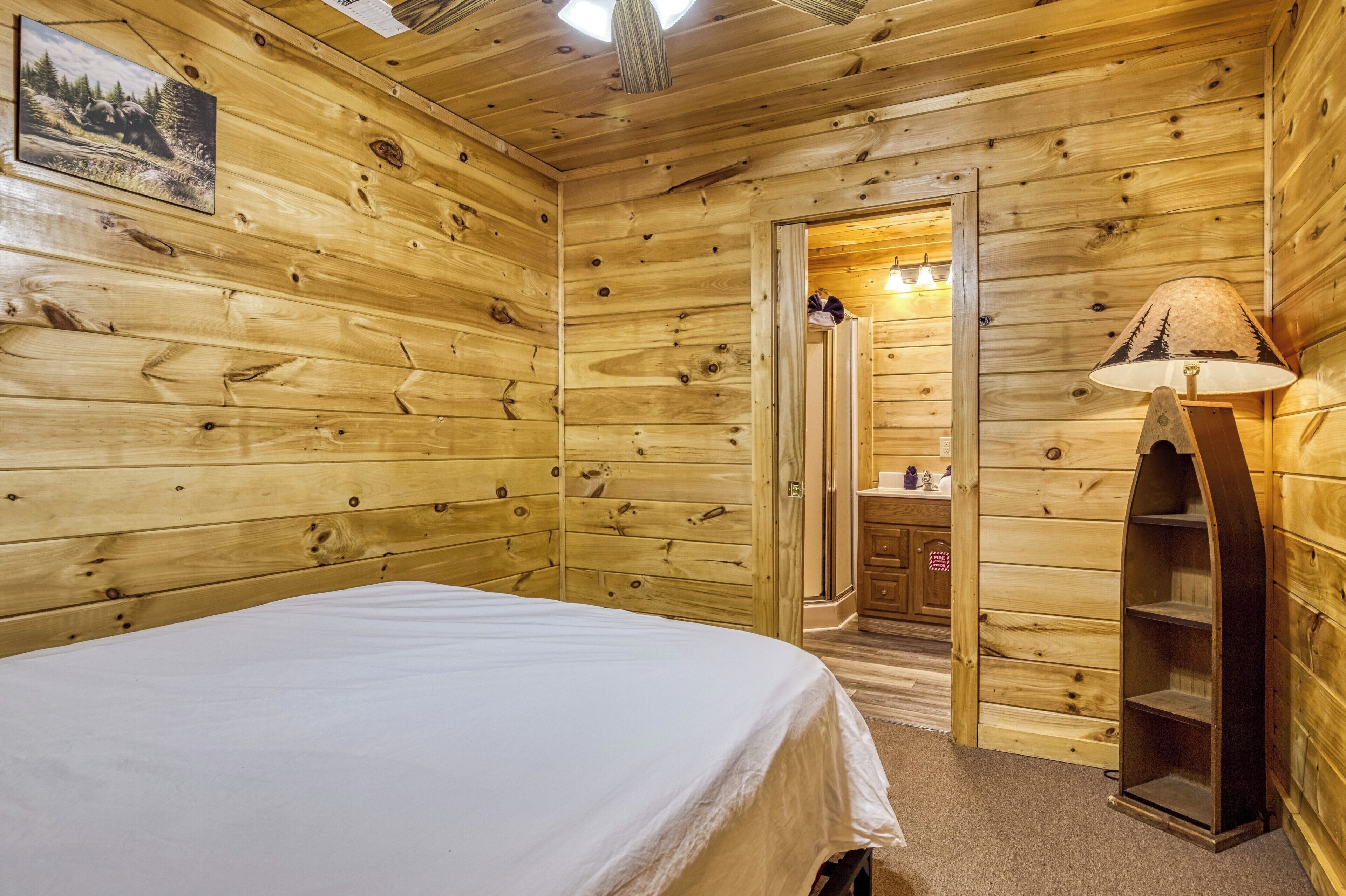 Une chambre rustique en bois, avec un lit, un miroir, une lampe et une porte donnant accès à une salle de bain.