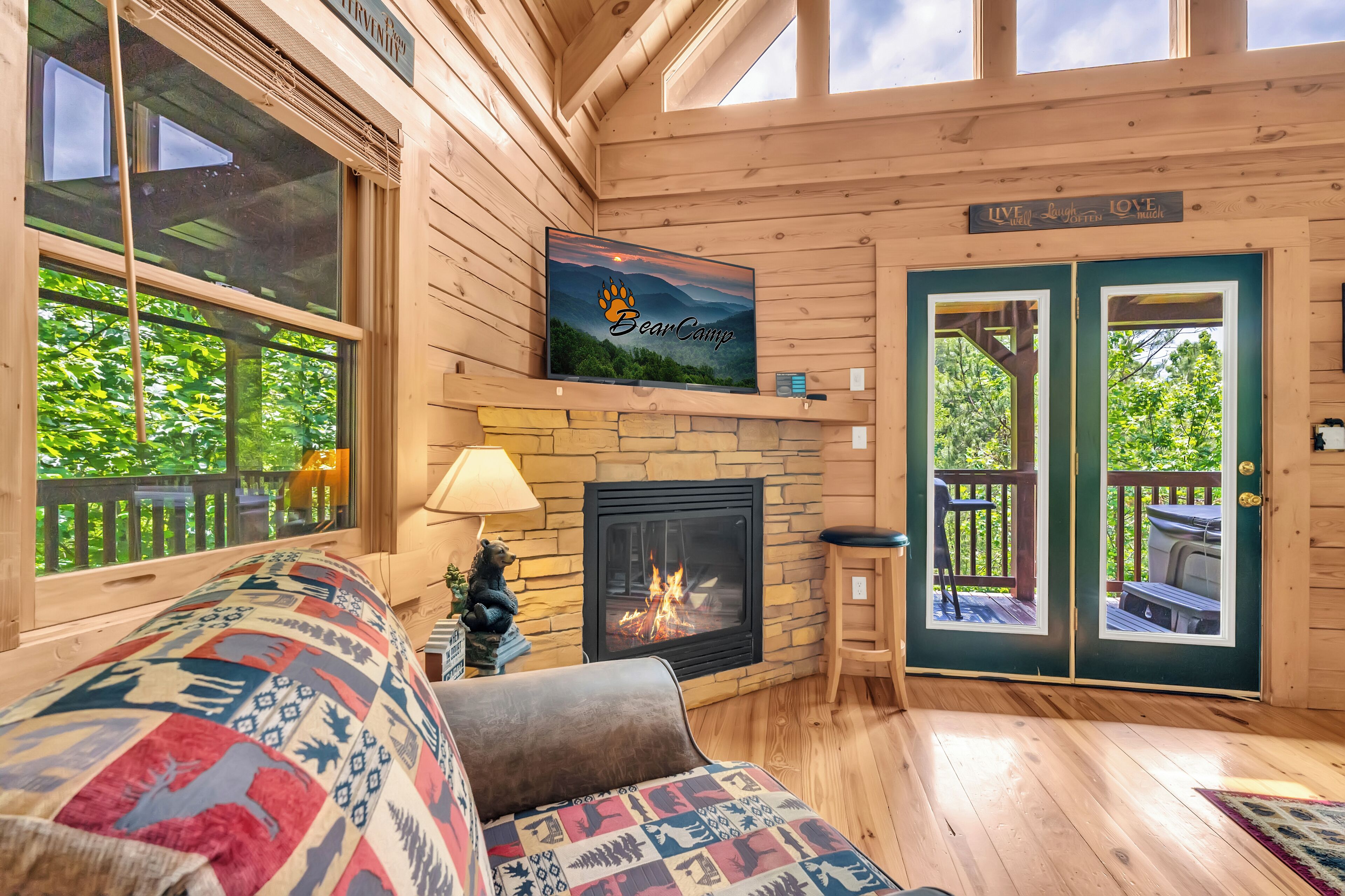 A cozy cabin interior with a fireplace, a couch with patterned cushions, and a sign reading "BearCamp".