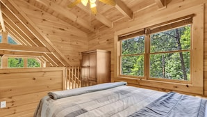 A wooden cabin bedroom with a large window, a bed, and a wardrobe.